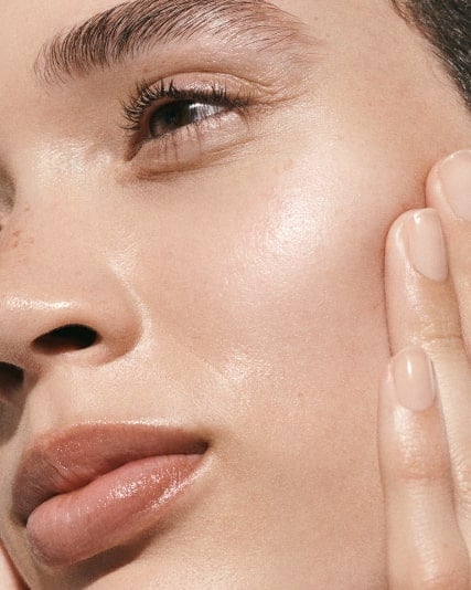 Model tilting her face to the side with hands pressed on cheeks.